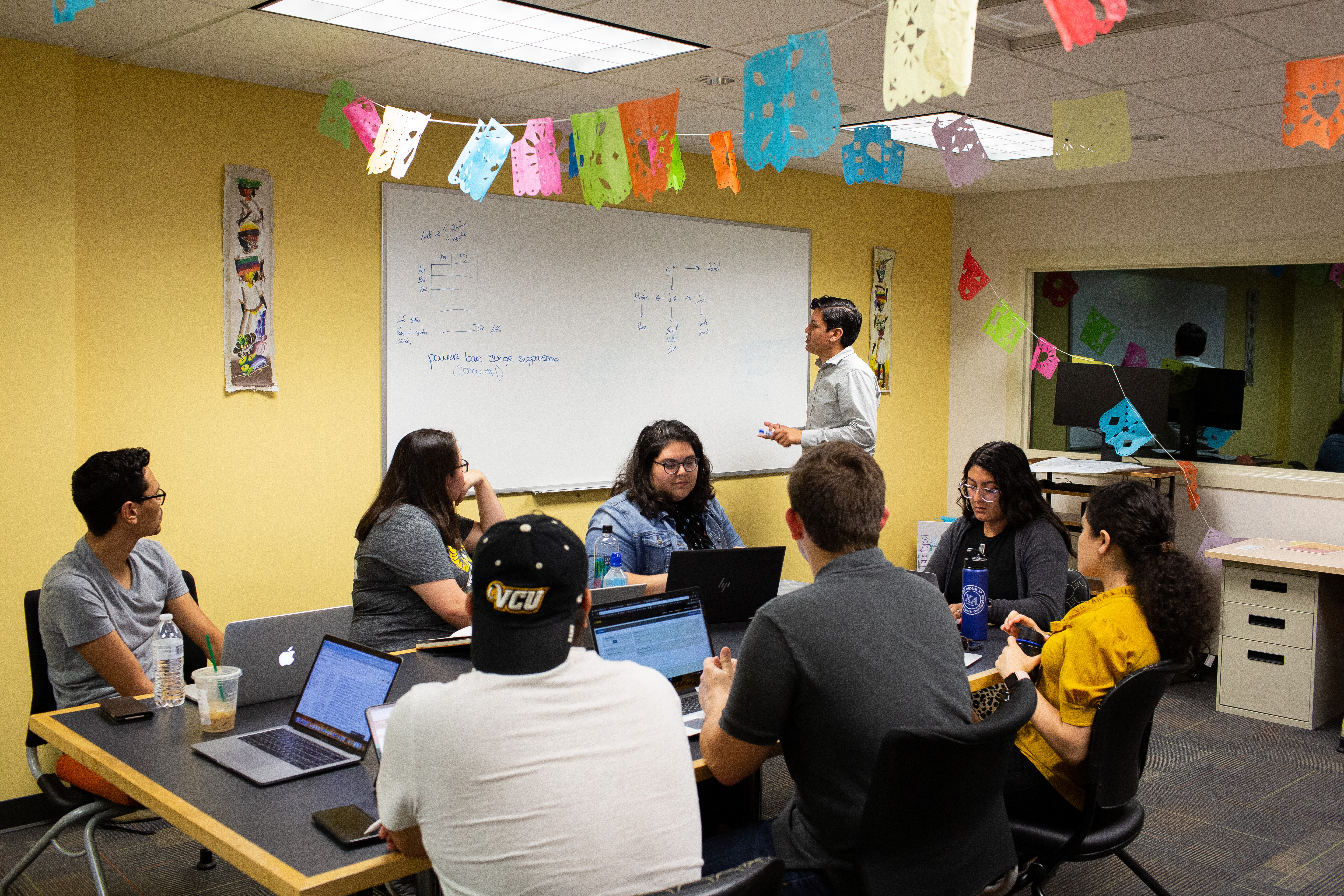 Students sitting together at a table taking notes while Oswaldo Moreno stands at a white-board